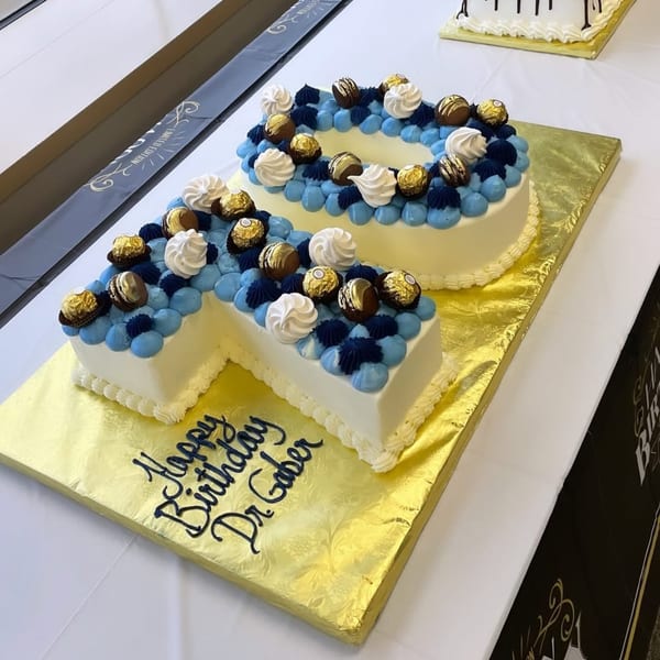 Number-shaped birthday cake decorated with blue and white frosting, chocolates, and meringues.