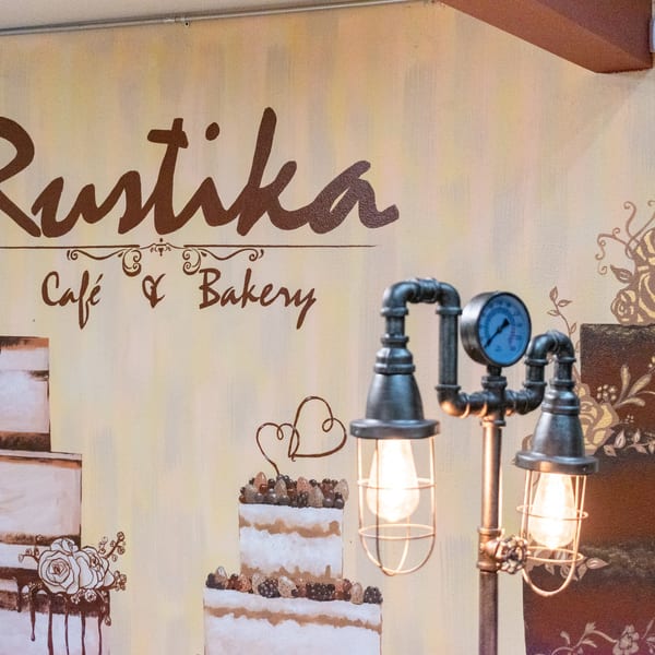A wall mural with "Rustika Cafe & Bakery" text, cake illustrations, and an industrial-style lamp.