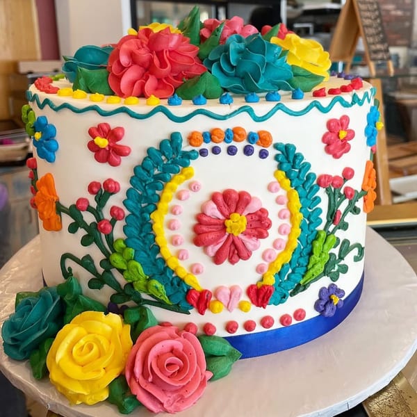 A white cake with vibrant floral icing decorations in red, yellow, blue, and green.