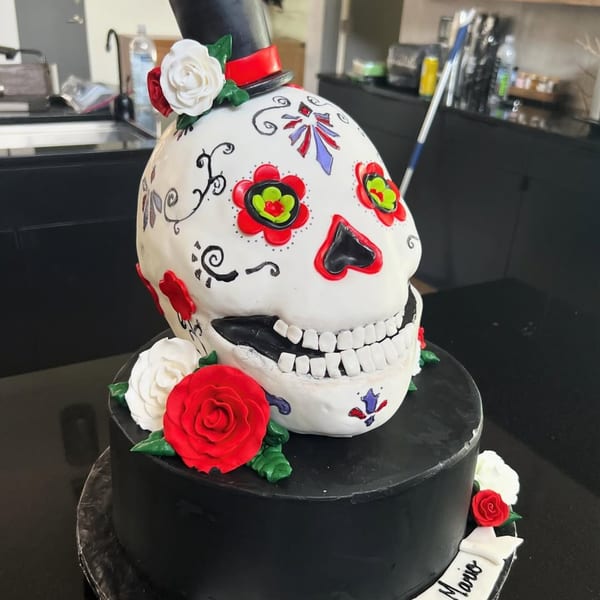A decorative Day of the Dead sugar skull cake with a top hat and red and white roses.