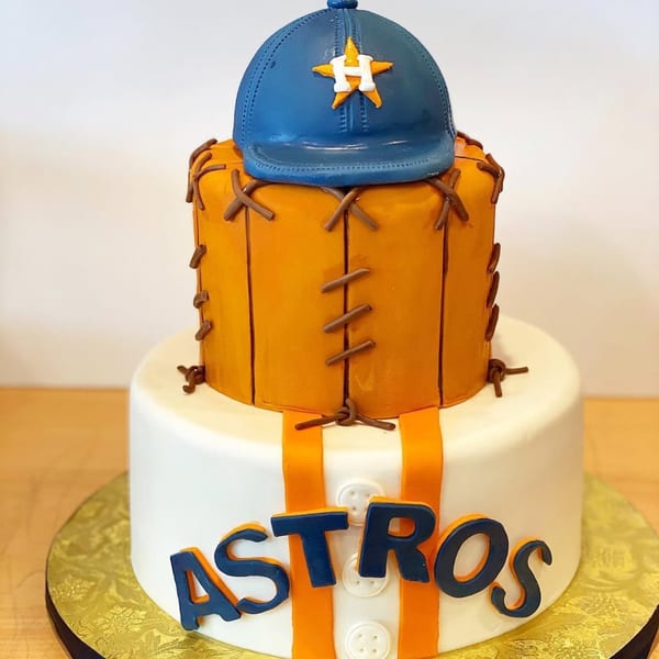 Two-tiered Houston Astros baseball cake with a blue cap, orange glove, and white jersey design.