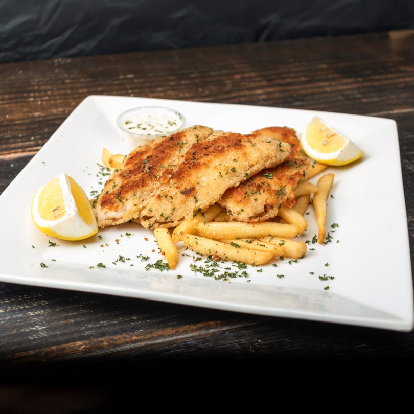 Crispy breaded fish fillets with french fries, lemon wedges, and tartar sauce on a white plate.