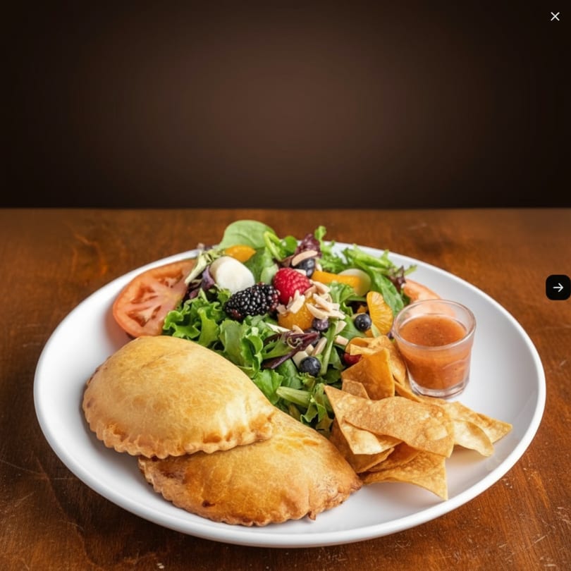Two golden empanadas, a fresh berry and citrus salad, tortilla chips, and salsa on a white plate.