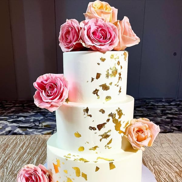 Three-tiered white cake with gold leaf accents and pink and peach roses, from Mama's Bistro Cafe and Bakery.