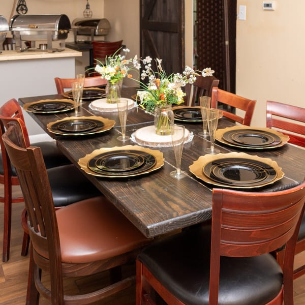 A long wooden table set with black and gold plates, champagne flutes, and floral centerpieces.